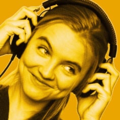 Yellow-filtered portrait of woman smiling looking to the side while wearing and holding headphones with both hands